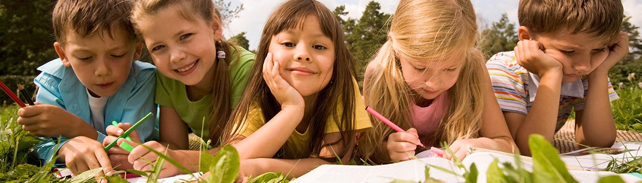 5 kids lying in the grass doing school work