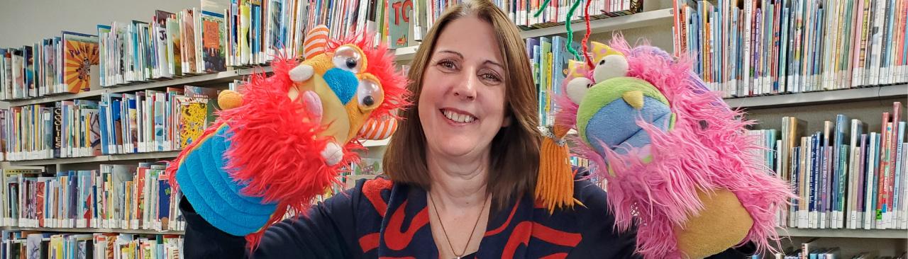 Trish, the children's program coordinator, smiling with two puppets.