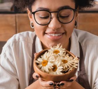 A teen holding a wooden bowl of dried flowers in a work space