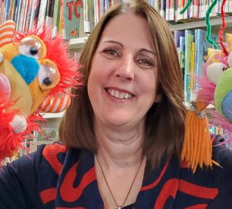 Trish, the children's program coordinator, smiling with two puppets.
