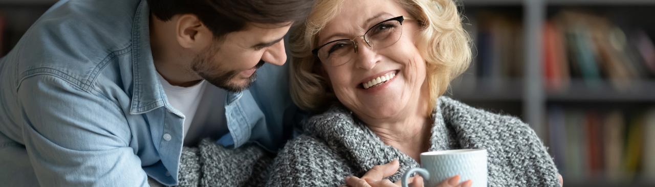 Care-for-caregivers.jpg A man hugging his adult mom who is cozy with tea and a blanket