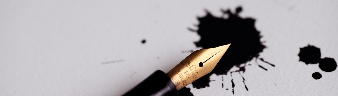 A fountain pen lying on paper with ink blotches