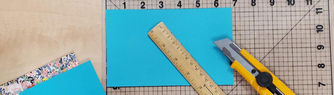 BookBinding_Hero.jpg A cutting mat, utility knife, and ruler with the cover and cover pages of a book being made