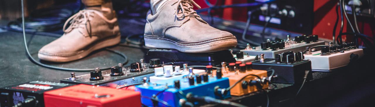 Custom-Guitar-Pedal-hero.jpg Someone's feet beside a row of guitar pedals