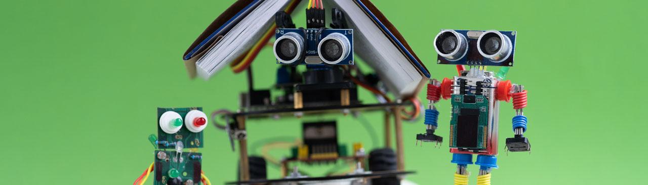Three robots standing on books. One has a book on it's head.